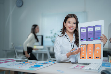 Young Asian woman UX designer creating and presenting mobile app wireframes, demonstrating UI and user experience design concepts in a modern digital office workplace