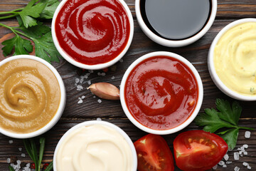 Different sauces, spices and herbs on wooden table, flat lay
