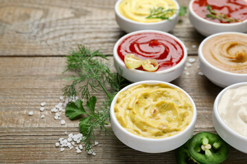 Different sauces and herbs on wooden table, closeup. Space for text