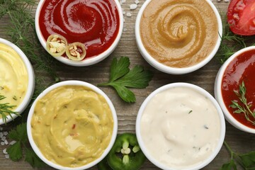 Different sauces and herbs on wooden table, flat lay