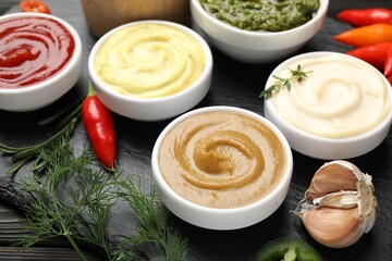 Different sauces and herbs on wooden table, closeup