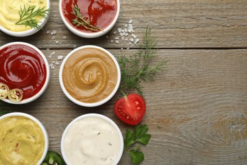 Different sauces and herbs on wooden table, flat lay. Space for text