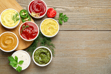 Different sauces and herbs on wooden table, flat lay. Space for text