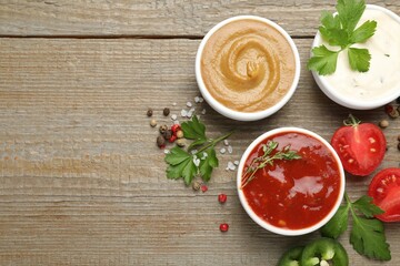 Different sauces, spices and parsley on wooden table, flat lay. Space for text