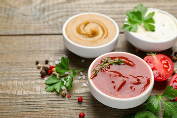 Different sauces, spices and parsley on wooden table, closeup. Space for text
