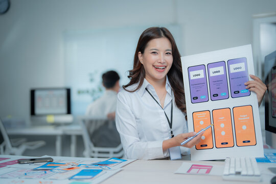 Young female UI UX designer presenting different wireframe layouts and screens for a new mobile application development project, working in a modern office - Powered by Adobe