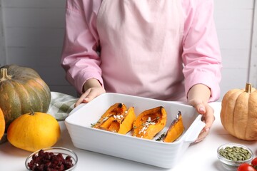 Woman with tasty baked pumpkin at white wooden table indoors, closeup
