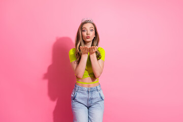 Cheerful young woman in a vibrant outfit blowing a kiss, showcasing a playful and charming expression against a pink backdrop
