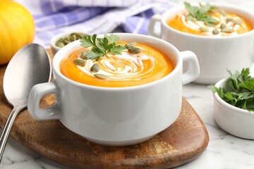 Tasty pumpkin cream soup with parsley and seeds served on light marble table, closeup