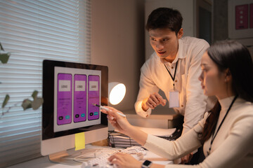 Asian design team collaborating on a mobile application user interface and user experience, working late perfecting the mockup screens on a computer display in a modern office
