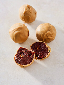 Delicious chocolate and peanut butter energy balls sit on a smooth surface. One energy ball is sliced in half to reveal its rich, dark filling. These snacks are perfect for a quick energy boost