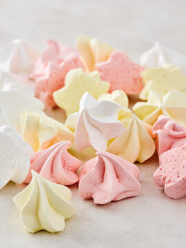 Delicate meringues in shades of pink, yellow, and white are beautifully arranged on a light surface. These sweet treats are perfect for any celebration or gathering