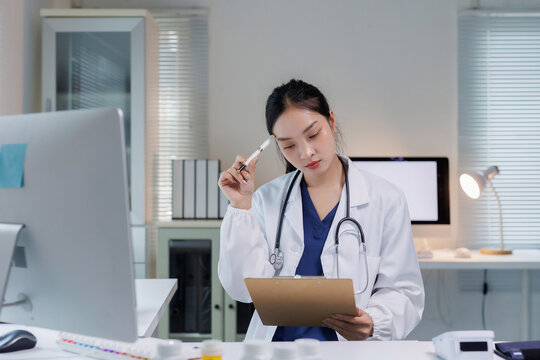 Asian female doctor thinking, reviewing medical documents at office desk. Healthcare professional concentrating on diagnosis
