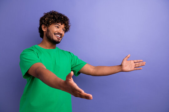 Confident young man in a green t-shirt gesturing with open arms in front of a violet-purple background - Powered by Adobe