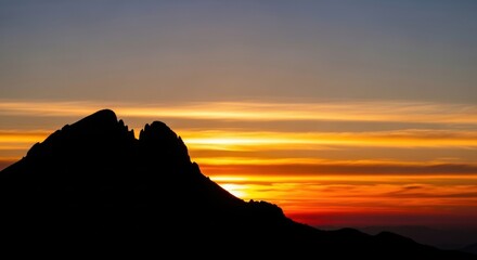Silhouette of a mountain peak against a vibrant sunset sky with orange and yellow hues