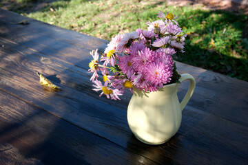 Fresh daisies in a cream pitcher on a rustic wooden table outdoors