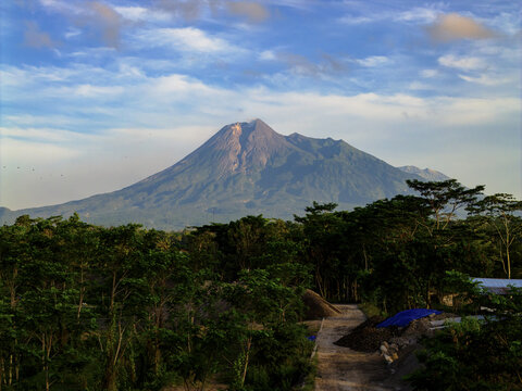 Aerial view of the majestic Mount Merapi rises above the lush green canopy, its peak kissed by the soft hues of the sky, Klaten, Central Java, Indonesia.