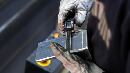 Precision measurement of metal part with caliper. Worker wearing gloves uses a digital caliper to...
