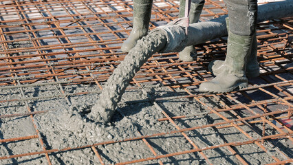 Concrete being poured over steel reinforcement grid. Workers in rubber boots pour wet concrete over a rusty rebar framework during the construction of a reinforced concrete floor. © Iryna