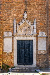 Obraz premium Gothic church entrance with stone relief in Venice. Elaborate Gothic-style church doorway in Venice, with weathered wooden doors and detailed stone religious relief above the entrance.