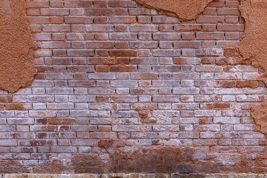Old Weathered Brick Wall with Peeling Plaster. Close-up of an aged brick wall with partially crumbling plaster and salt stains, revealing texture and urban decay.