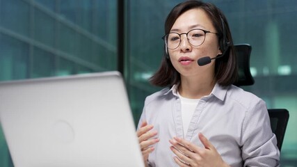 Confident asian businesswoman in wireless headset talking on video call conference using a laptop sitting in office. Female coach speaks remotely, communicates at online meeting or training. Close up - Powered by Adobe