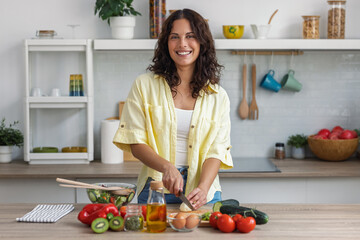 Pretty woman cutting fresh vegetables while preparing healthy salad in the kitchen at home.