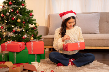 Adult Woman with Santa Hat Unwrapping Christmas Present by Christmas Tree in Cozy Home Holiday Celebration Festive Season Gift Giving Concept