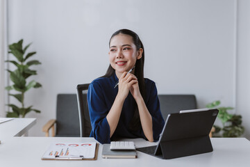 Asian businesswoman working in office, holding pen and smiling, planning strategy and analyzing data on charts