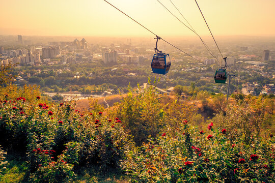 Scenic view of the Kok-Tobe cable car gondolas reaching the hilltop, with the city of Almaty, Kazakhstan, glowing in the evening sun in the background
