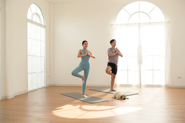 Fototapeta premium Couple Practicing Yoga at Home With a Dog Resting on the Floor in Natural Light