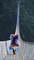 the porter carrying extremely large of colourful  bundle clothes across a narrow ,long  and high bridge over the deep green valley at Nepal. the strength and preseverence of human.