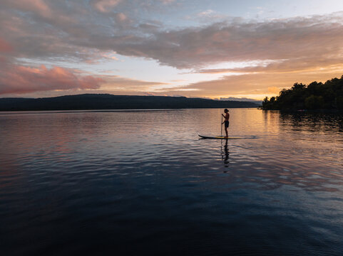 Aerial view of a lone paddleboarder glides across the tranquil waters as the sun paints the sky with fiery hues, Moso island, Shefa Province, Vanuatu.