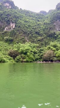 Vertical 4K video of a quiet boat trip on the Trang An river in Ninh Binh surrounded by beautiful mountains and lush greenery outdoor at daytime in Vietnam while traveling in Asia.