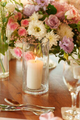 A beautifully arranged table features a glowing candle in glass and vibrant flowers in soft pastel colors, creating a serene setting for a special occasion dinner.