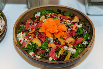 A fresh salad is displayed in a wooden bowl, featuring mixed greens, colorful fruits, and edible flowers. It adds a healthy and vibrant touch to a gathering's table.