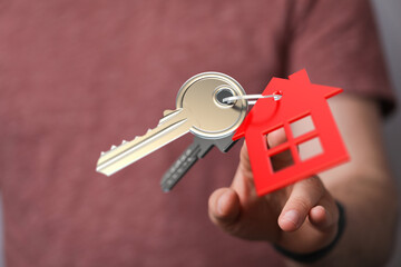 Close up of hand holding keys with a red house tag, symbolizing home ownership, property, real estate, and the dream of a new home. Perfect for