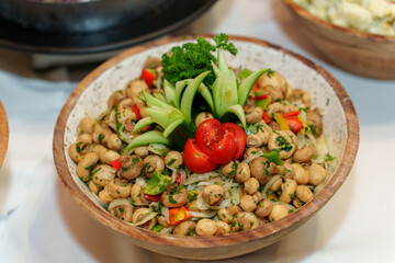 A vibrant salad featuring beans, fresh tomatoes, cucumbers, and herbs is beautifully arranged in a wooden bowl, showcasing a healthy dining option at an event.