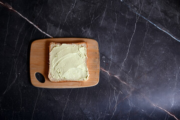 square table of bread with spread avocado butter on wooden board on dark background