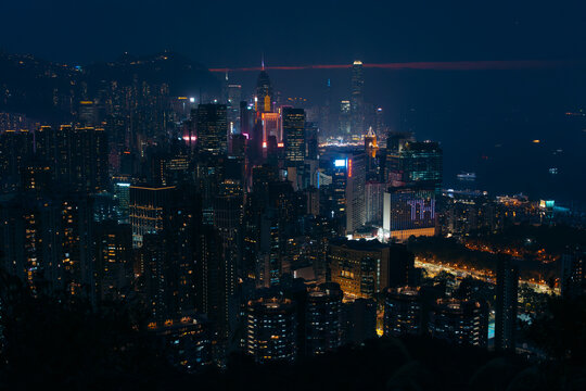 Aerial view of a vibrant metropolis where a symphony of illuminated skyscrapers pierce the dark sky, reflecting on the tranquil harbor waters, Hong Kong, Hong Kong.