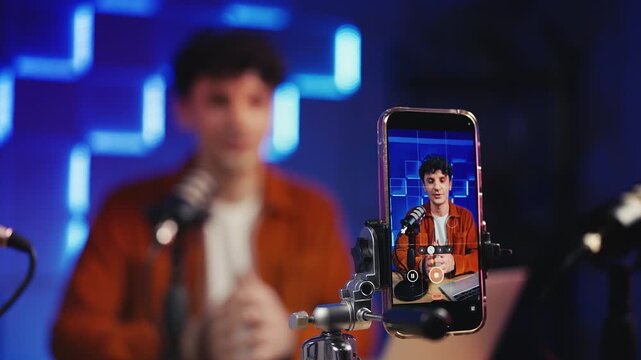 Happy male podcaster recording vlog on smartphone in studio, content creator