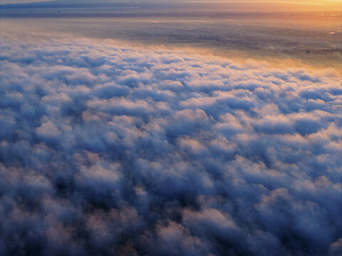 Aerial view of a celestial ocean of clouds blanketing the land below, with the horizon kissed by the warm glow of the sun, Karanganyar Regency, Central Java, Indonesia.