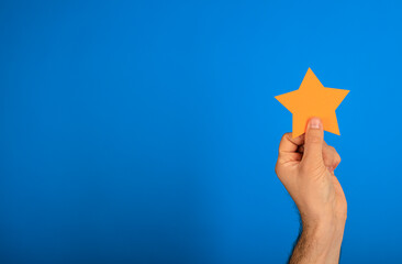 A hand holding an orange star cutout against a vibrant blue background, conveying concepts of...