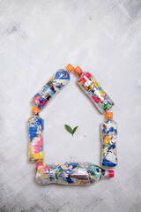 Five pet plastic bottles filled with compressed plastic waste arranged in the shape of a house with green leaves inside