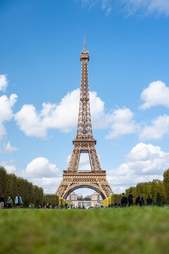 View of the majestic Eiffel Tower piercing the blue sky dotted with fluffy clouds, framed by lush greenery, a timeless symbol of romance, Paris, Ile-de-France, France.