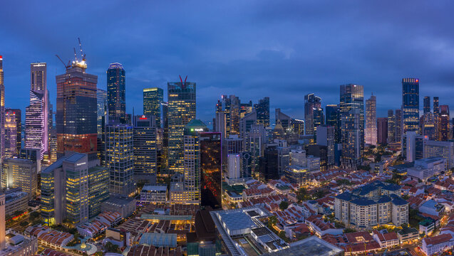 Aerial view of a glittering cityscape where towering skyscrapers pierce the twilight sky, their lights reflecting off the dark waters of Marina Bay, Singapore, Singapore.