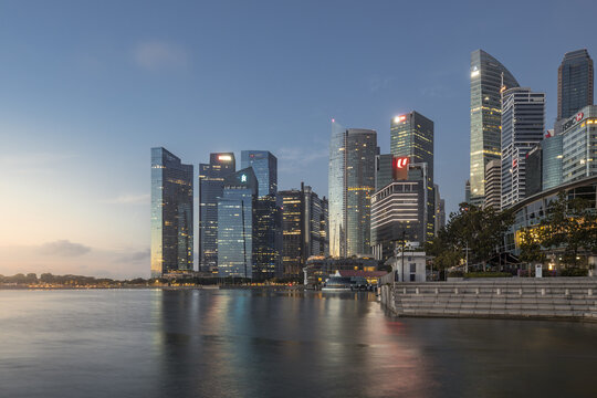 View of gleaming skyscrapers reflecting the tranquil waters of Marina Bay under a soft dusk sky, creating a mesmerizing urban landscape, Singapore, Singapore.