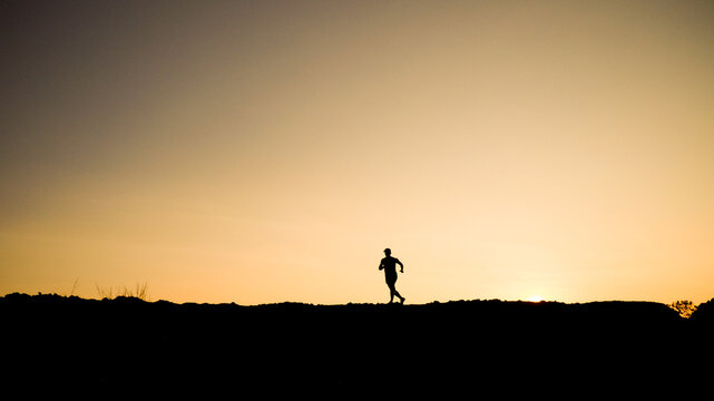 A silhouette of a runner training during sunset. A lone athlete exercises amidst nature, bathed in warm hues