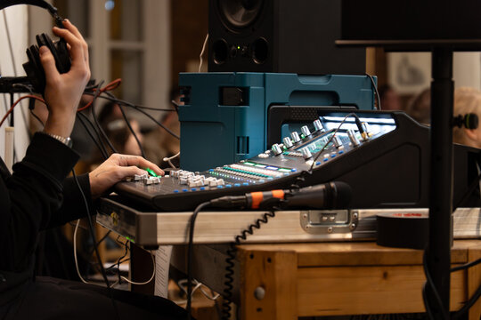 Sound engineer operating professional audio mixing console during live concert or event – adjusting sound levels with headphones in studio or venue - Powered by Adobe