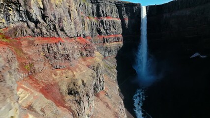 Close drone shot of Hengifoss waterfall in East Iceland. The steep canyon reveals layers of red volcanic rock and dark basalt columns. - Powered by Adobe